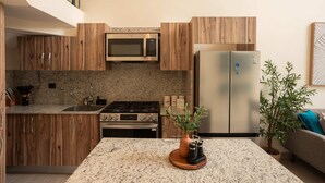 Cocina moderna con armarios de madera, electrodomésticos de acero inoxidable, encimeras de granito y una isla central con estación de café.