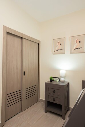 Ein Zimmer mit einem Holzschrank, einem Nachttisch mit Lampe und zwei gerahmten Bildern an der Wand.