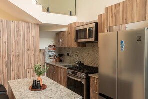 Eine moderne Küche mit Holzschränken, einem Edelstahlkühlschrank, einer Mikrowelle und einem Gasherd.
