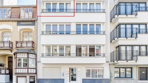 Un immeuble résidentiel à plusieurs étages, doté d’un portail de garage, de grandes fenêtres et de balcons.