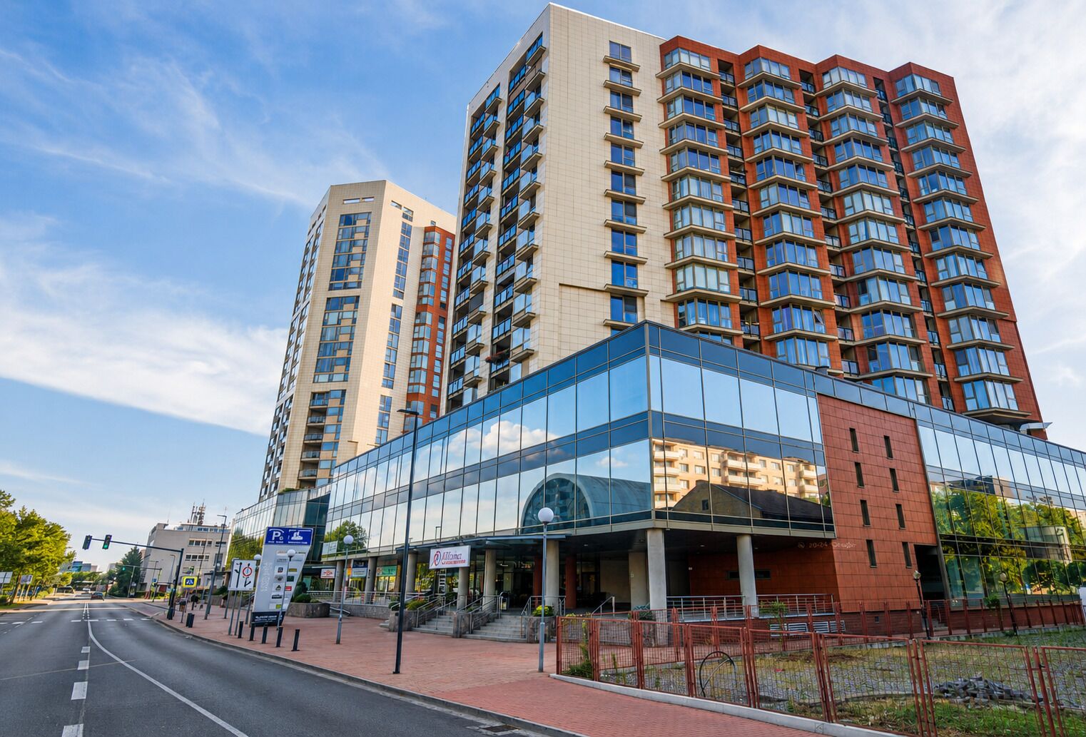 A modern multi-story hotel with a glass facade, a parking sign, and a pedestrian walkway.