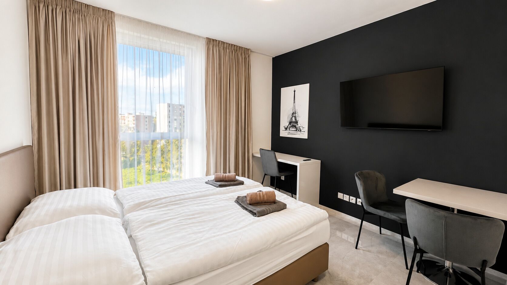 Ett hotellrum med en stor säng, ett skrivbord, en stol, en platt-TV och ett fönster med gardiner.
