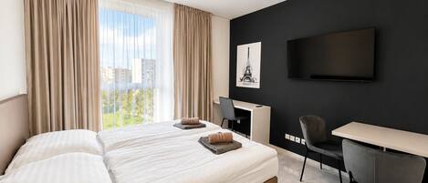 A hotel room with a large bed, a desk, a chair, a flat-screen TV, and a window with curtains.