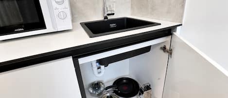 A kitchen with a built-in microwave, a black sink, and a stainless steel range hood.