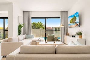 A modern living room with a sofa, a coffee table, and a television mounted on the wall. - Private Pool | 2BR Retreat | Near Eagle Beach (Noord)