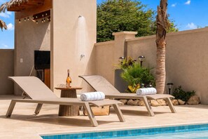 A poolside area with two lounge chairs, a bottle of wine, and a small table. - Private Pool | 2BR Retreat | Near Eagle Beach (Noord)