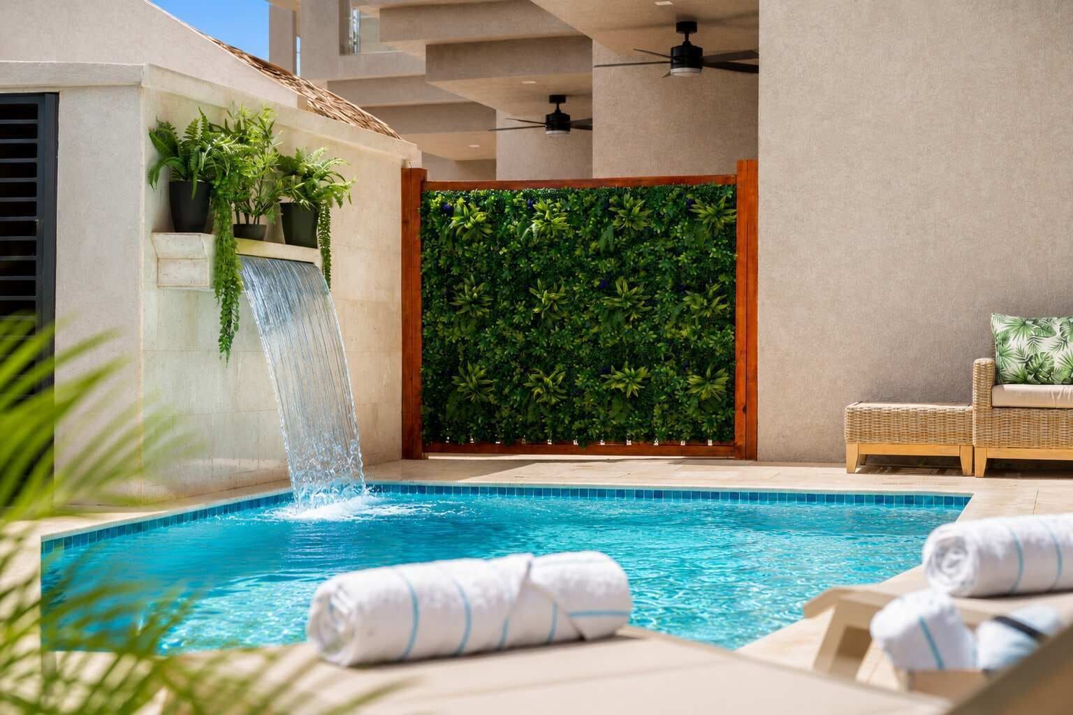 Une piscine agrémentée d’une cascade, entourée de chaises longues et bordée d’un mur végétal.