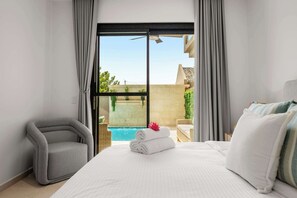 Ein Hotelzimmer mit Bett, Sessel, Blick auf einen Pool und einem Balkon.