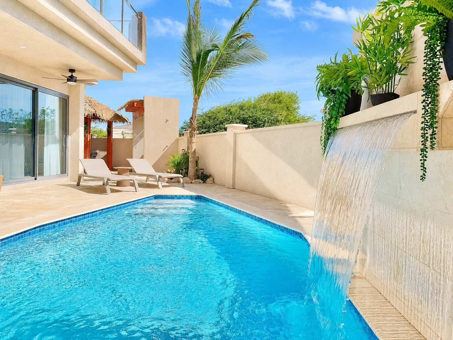 A swimming pool with lounge chairs, a palm tree, and a thatched-roof structure.