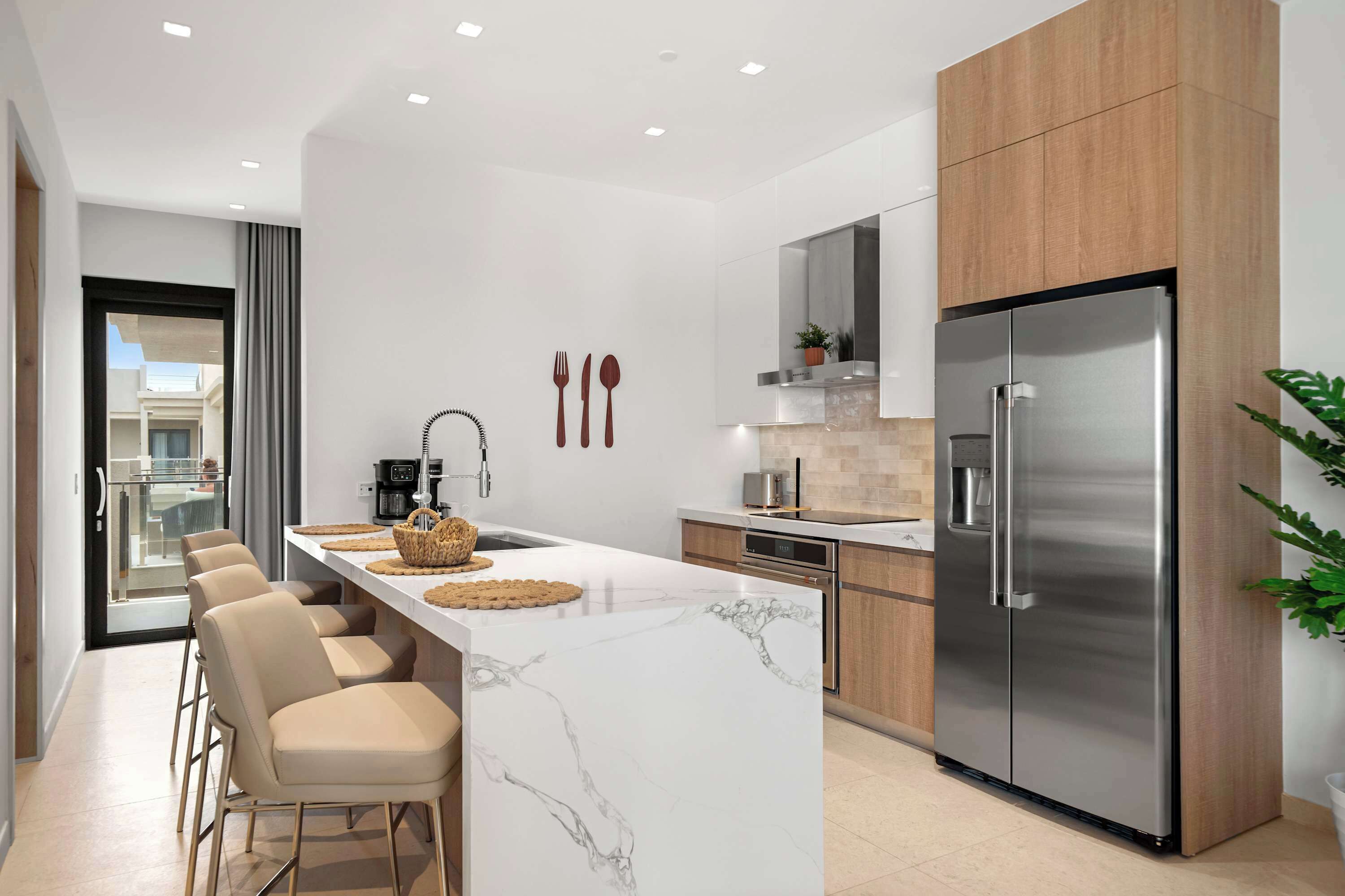 A modern kitchen with a marble island, stainless steel appliances, and a view to the outside.