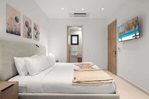 A modern bedroom with a large bed, a television on the wall, and artwork above the bed. - Breezy Balcony | Top-Floor 1BR | Near Eagle Beach (Noord)