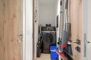 A laundry room with a washing machine, a dryer, and a vacuum cleaner. - Breezy Balcony | Top-Floor 1BR | Near Eagle Beach (Noord)