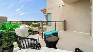 A balcony with a glass railing, a black wicker chair, a small round table, and a potted plant. - Breezy Balcony | Top-Floor 1BR | Near Eagle Beach (Noord)
