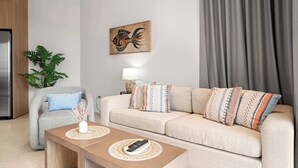 A modern living room with a sofa, a chair, a table, a plant, a painting, and a lamp. - Breezy Balcony | Top-Floor 1BR | Near Eagle Beach (Noord)
