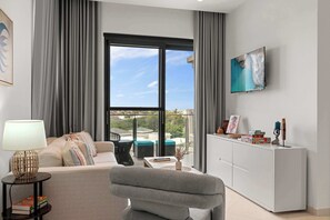 A modern living room with a sofa, a coffee table, a lamp, and a TV mounted on the wall. - Breezy Balcony | Top-Floor 1BR | Near Eagle Beach (Noord)
