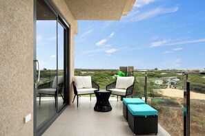 A balcony with a glass door, two chairs, a small table, and a sofa. - Breezy Balcony | Top-Floor 1BR | Near Eagle Beach (Noord)
