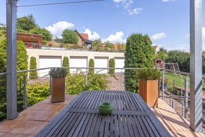 A wooden deck with a table and chairs, surrounded by metal railings and potted plants. - Apartment W2: Romantic Luxury for 2 / Covered Balcony, Private Whirlpool & Fireplace (Diemelstadt)