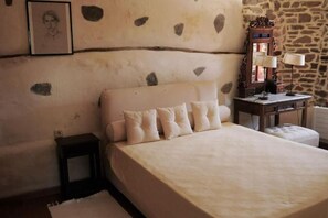 A bedroom with a bed, pillows, a nightstand, a lamp, and a mirror.