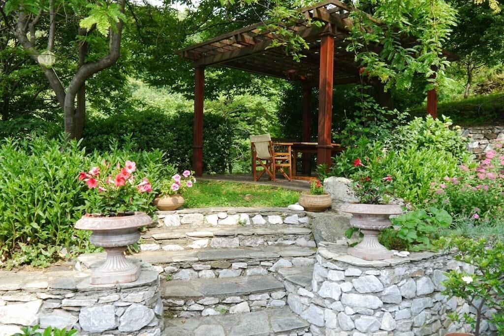 Um jardim com pérgola, degraus de pedra e plantas em vasos.