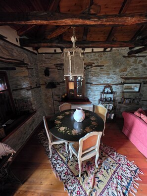 A rustic room with a stone wall, wooden beams, a round table with a vase, and a patterned rug.