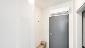 A room with a grey door, a beige chair, and a white wall with an air conditioning unit mounted above the door. - 1 room Apartment with AC, Vienna Gate 2 (Bratislava)