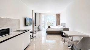 A modern hotel room with a kitchenette, a bed, a dining area, and a large window with a city view. - 1 room Apartment with AC, Vienna Gate 2 (Bratislava)