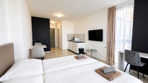 Hotellihuone, jossa on sänky, työpöytä, tuoli, televisio ja pieni keittiö.
