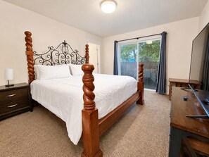 A bedroom with a four-poster bed, a nightstand, a desk, and a large window with curtains. - Unwind at Midtown Haven (Coeur d'Alene)