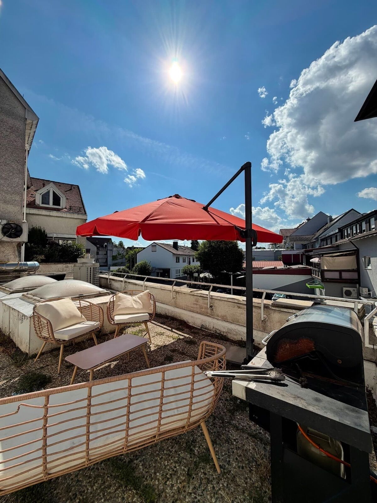 Eine Dachterrasse mit Gartenmöbeln, einem Grill und einem roten Sonnenschirm.