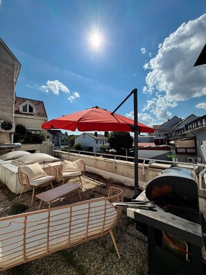 A rooftop patio with outdoor furniture, a grill, and a red umbrella. - Designer apartment with a 40 m² rooftop terrace – Achern, gateway to the Black Forest (Achern)