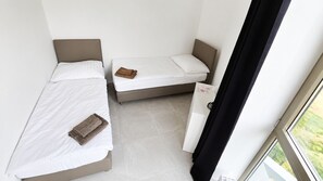 A small, compact room with two beds, a small cabinet, and a window. - 2 room Apartment with AC, Vienna Gate 4 (Bratislava)