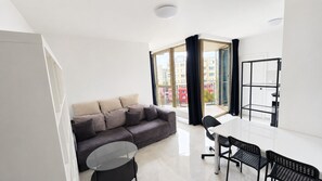 A modern living room with a sofa, a round glass coffee table, and a dining area with a white table and black chairs. - 2 room Apartment with AC, Vienna Gate 4 (Bratislava)