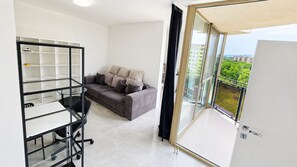 A modern apartment with a balcony, a grey sofa, and a glass door leading to the balcony. - 2 room Apartment with AC, Vienna Gate 4 (Bratislava)