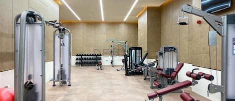 Uma academia com diversos equipamentos de exercícios, incluindo aparelhos de musculação e pesos livres, dispostos em um espaço amplo.