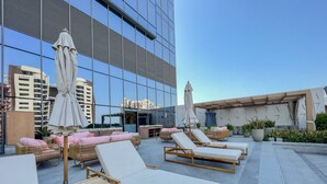 Eine Dachterrasse mit Liegestühlen und Sonnenschirmen, im Hintergrund ein modernes Gebäude und Kübelpflanzen.