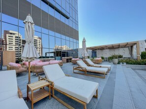 Eine Dachterrasse mit Liegestühlen und Sonnenschirmen, im Hintergrund ein modernes Gebäude und Kübelpflanzen.