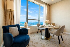 A hotel room with a large window, a blue armchair, a dining table with chairs, and a view of a bridge. - Sea-Facing Studio with Panoramic Palm Views from a High Floor, Near Atlantis (Dubai)
