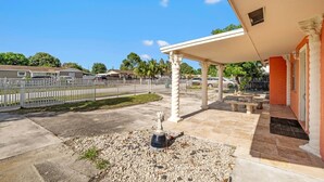 A covered outdoor area with a white fence, a stone patio, and a small garden with a planter. - Miami Gardens Pool Retreat (Miami Gardens)
