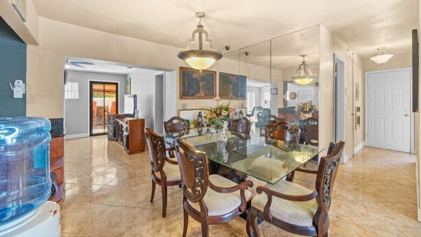 A spacious dining area with a glass table surrounded by ornate chairs, a large mirror on the wall, and a ceiling fan. - Miami Gardens Pool Retreat (Miami Gardens)