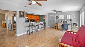A spacious living area with a kitchen, a dining area with bar stools, a red sofa, and ceiling fans. - Miami Gardens Pool Retreat (Miami Gardens)