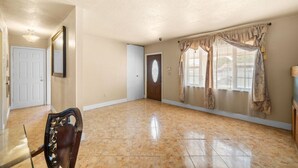 A spacious room with a polished tile floor, a door with a decorative glass panel, and a window with patterned curtains. - Miami Gardens Pool Retreat (Miami Gardens)