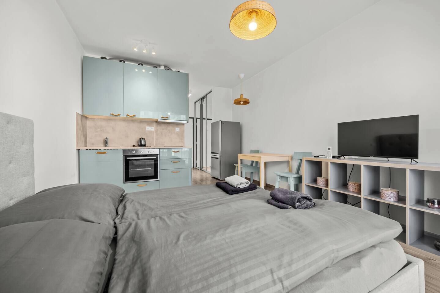 Un dormitorio moderno con una cama grande, un kitchenette, un televisor y un espacio de trabajo.