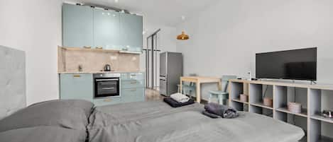 Un dormitorio moderno con una cama grande, un kitchenette, un televisor y un espacio de trabajo.