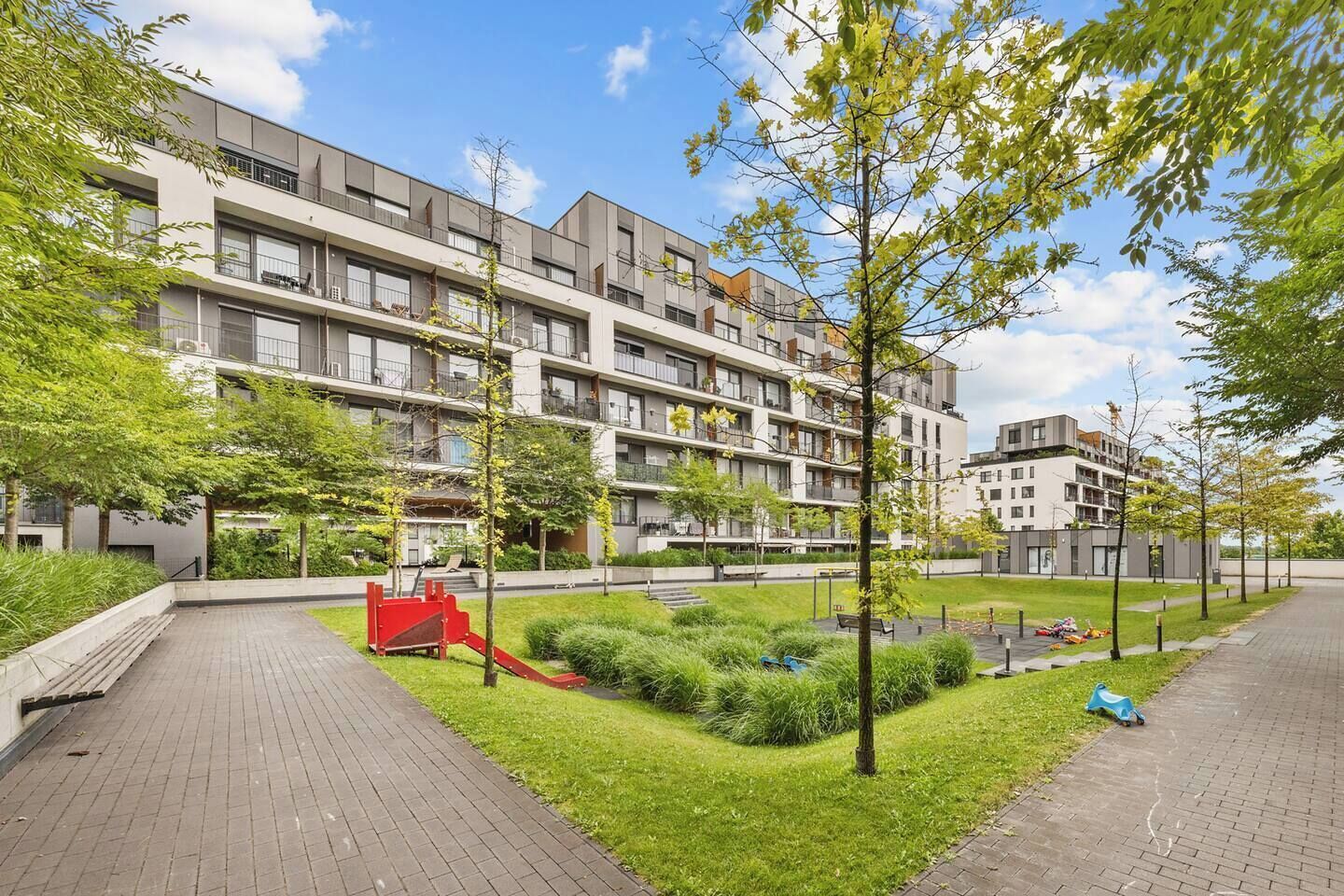 A multi-story residential building with balconies, a playground, and a well-maintained lawn.