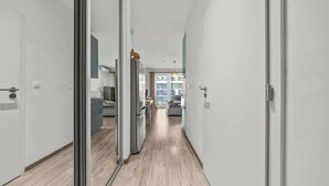 Un passadís modern amb portes de vidre que donen a una cuina i zona d'estar, amb terra de fusta i decoració minimalista.