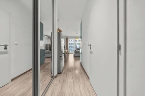 Ein moderner Flur mit Glastüren zu einer Küche und einem Wohnbereich, mit Holzboden und minimalistischer Einrichtung.