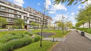 Un edifici d'apartaments modern amb un camí pavimentat, zones verdes i un cel serè.