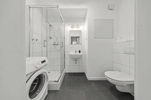 A modern bathroom with a glass-enclosed shower, a washing machine, a sink, and a toilet.