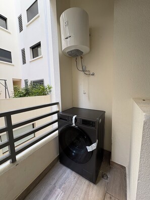 Zona de lavandería con lavadora y calentador de agua en un balcón.