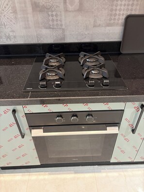 A kitchen with a gas stove and oven, a backsplash with a geometric pattern, and a countertop with a dark surface. - New luxury apartment near stadium (Tanger)